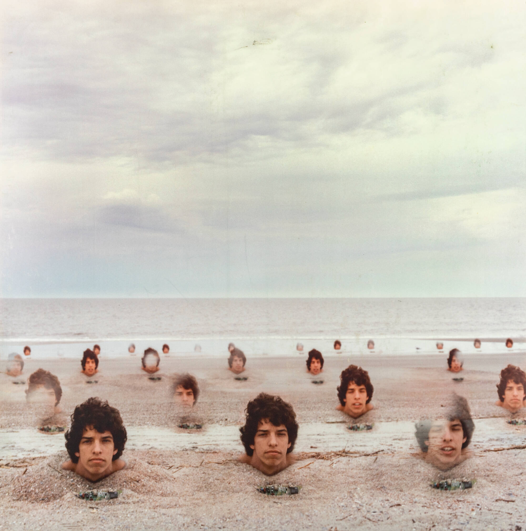 Photograph of heads poking out of a sandy beach landscape.